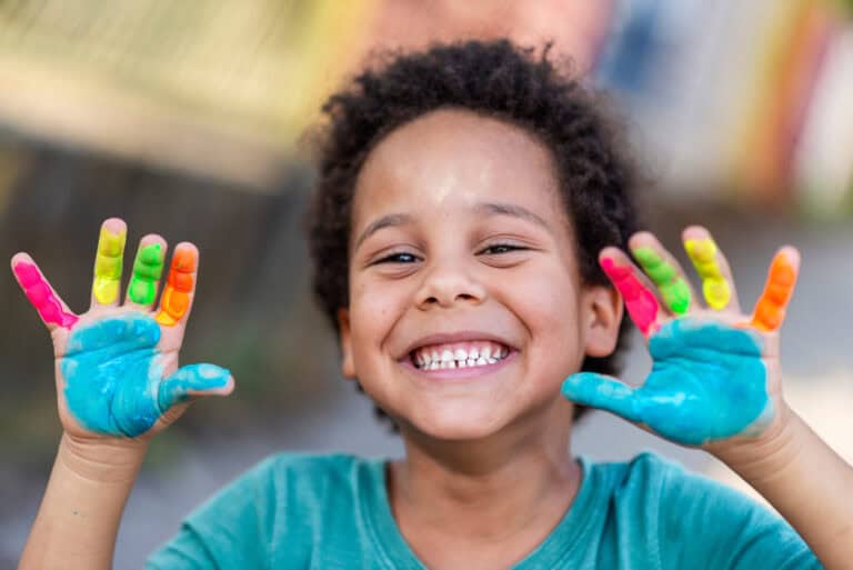 A boy with painted hands smiles at the camera