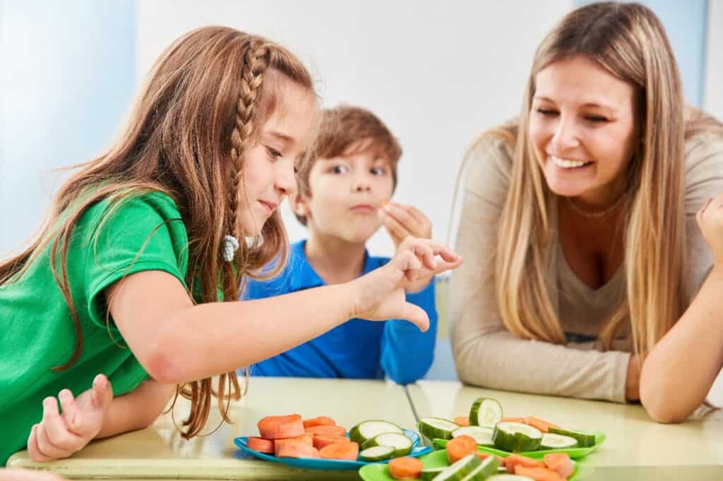 A woman and two children share a plate of veggies