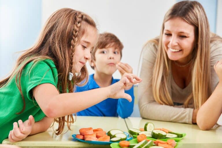 A woman and two children share a plate of veggies