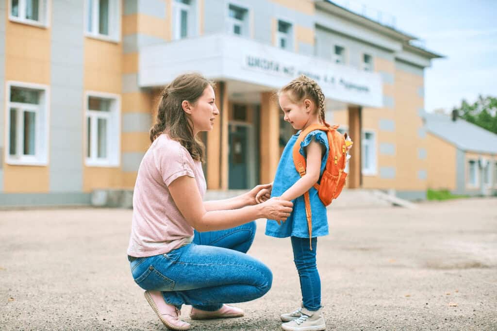A woman crouches to speak with a child in front of an elementary school