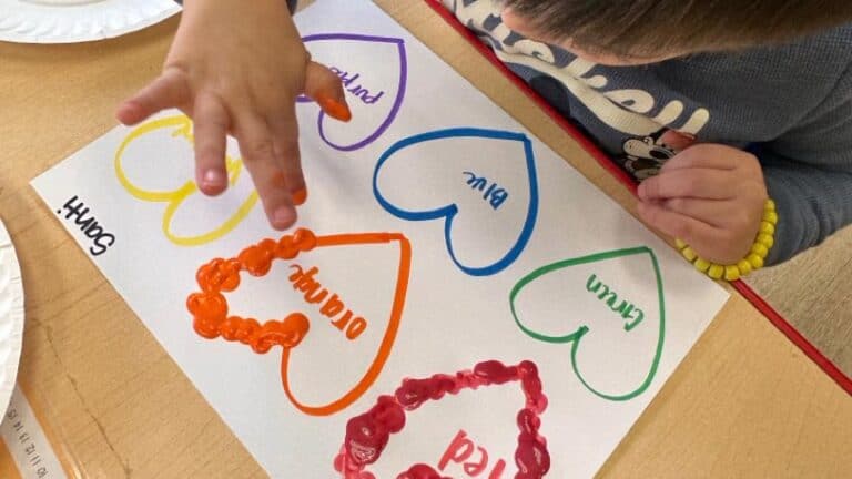 A child makes finger paint art of colorful hearts