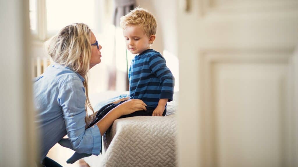 A boy sits on a bed and is scolded by his mother