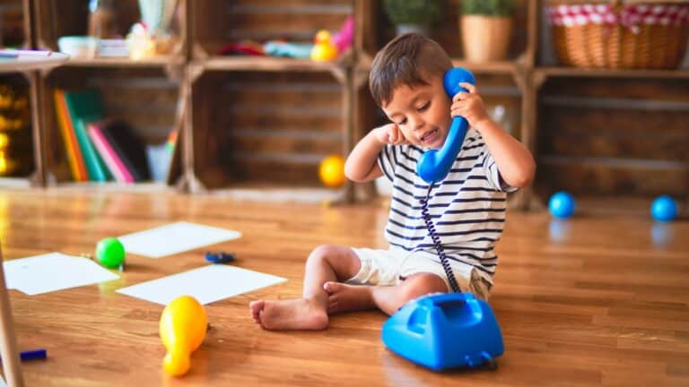 A young boy sits on the floor playing with a toy telephone