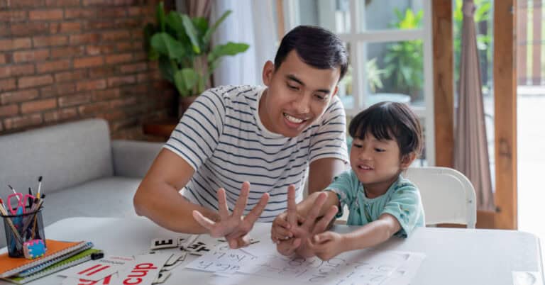 A father helps his son practice counting on his fingers