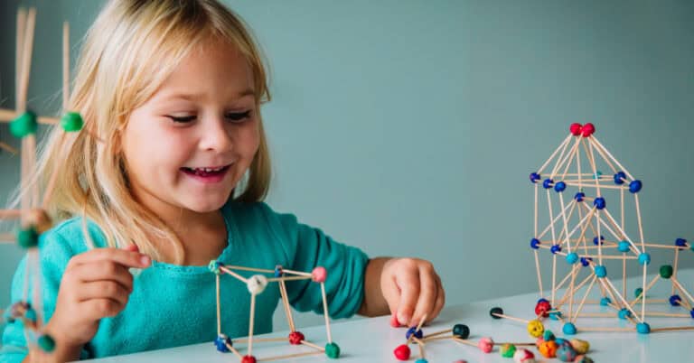 A girl smiles while making a tower with toothpicks and little ball Play Doh balls