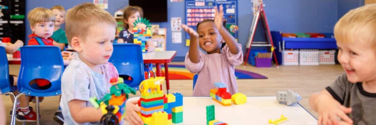 Three preschoolers playing with building blocks at a table.