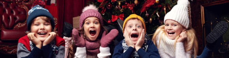 Four children in winter hats and coats lying on floor in front of Christmas tree.