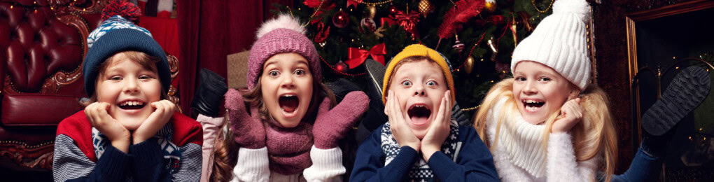 Four children in winter hats and coats lying on floor in front of Christmas tree.