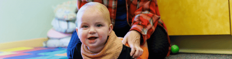 smiling baby crawling on the floor in front of a caretaker