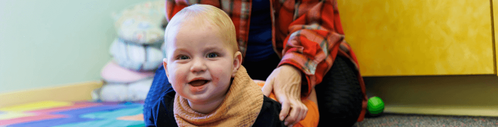 smiling baby crawling on the floor in front of a caretaker