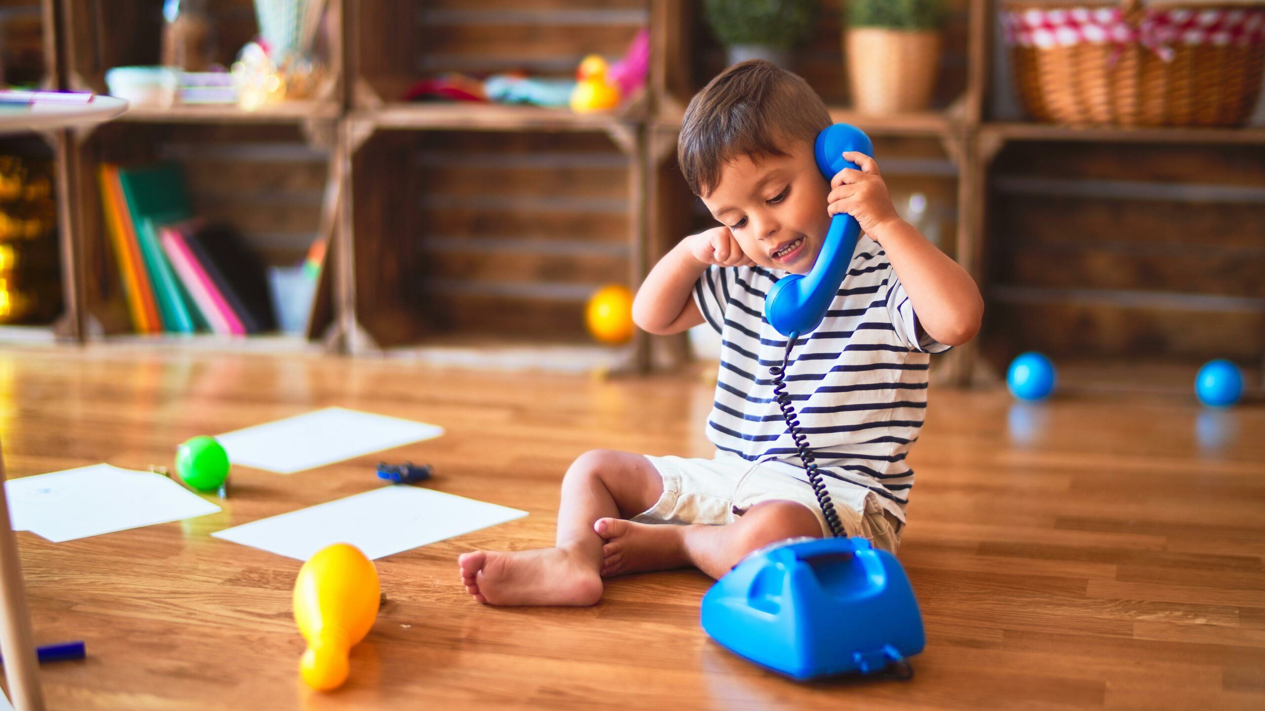 Preschool boy talks on pretend blue phone in classroom.