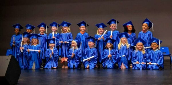 class of pre-k students in blue graduation cap and gowns with diplomas
