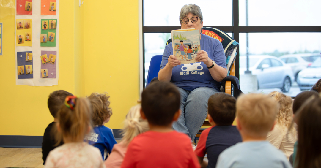 Teacher reading a book to a preschool class sitting on the floor.