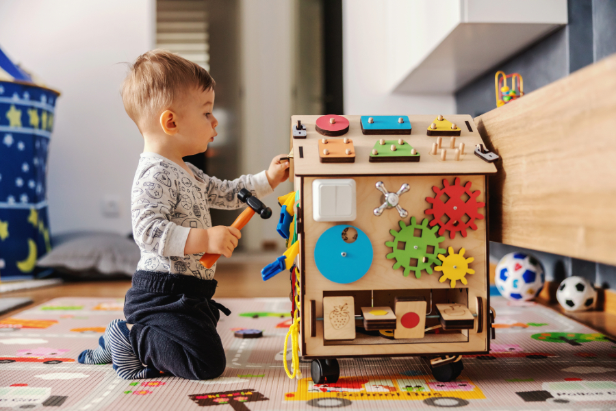 Toddler boy playing with a toy house covered in gears and peg blocks.