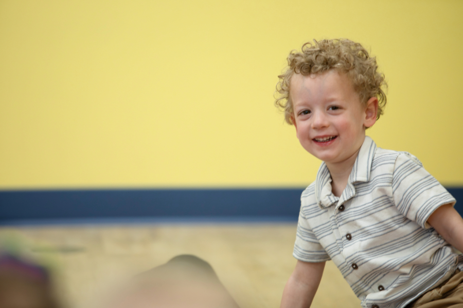 Preschool boy sitting on floor and smiling.